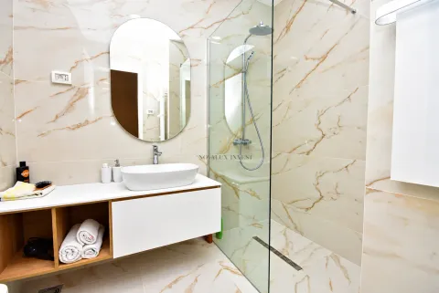 Modern bathroom with a washbasin, mirror, and walk-in shower finished with marble tiles. - image 9