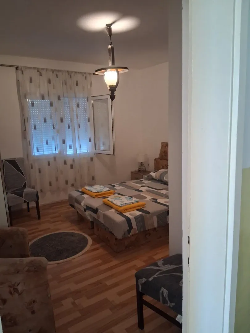 Spavaća soba sa bračnim krevetom, prozorom i laminatnim podom.