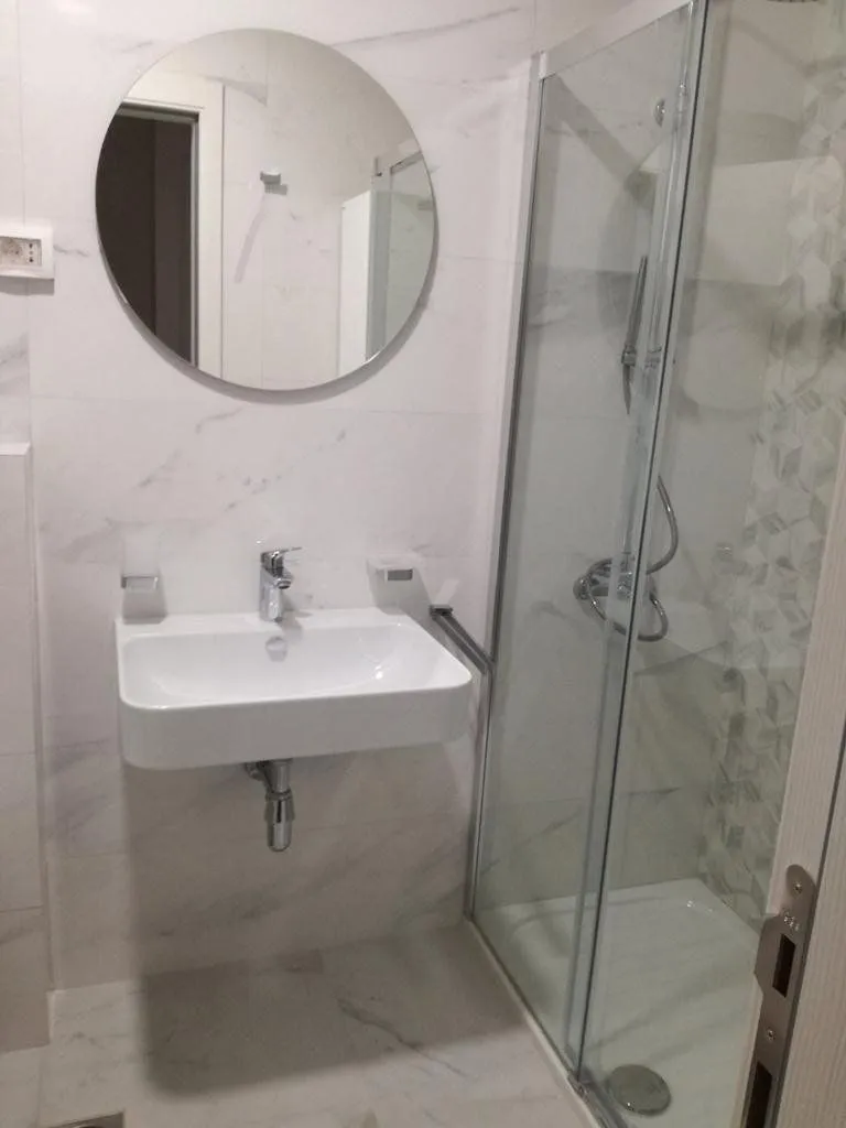 Modern bathroom with a shower enclosure, washbasin, and round mirror.