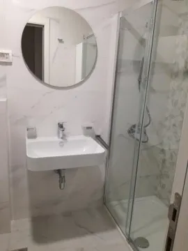 Modern bathroom with a shower enclosure, washbasin, and round mirror. - image 4