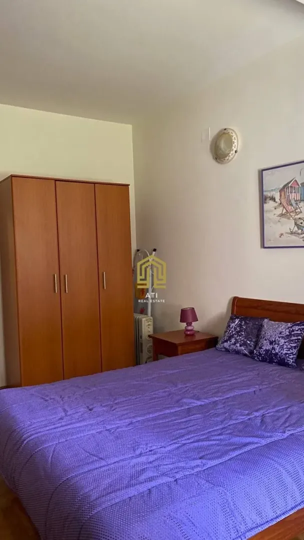 Spavaća soba sa bračnim krevetom, drvenim ormarom i noćnim stočićem.
