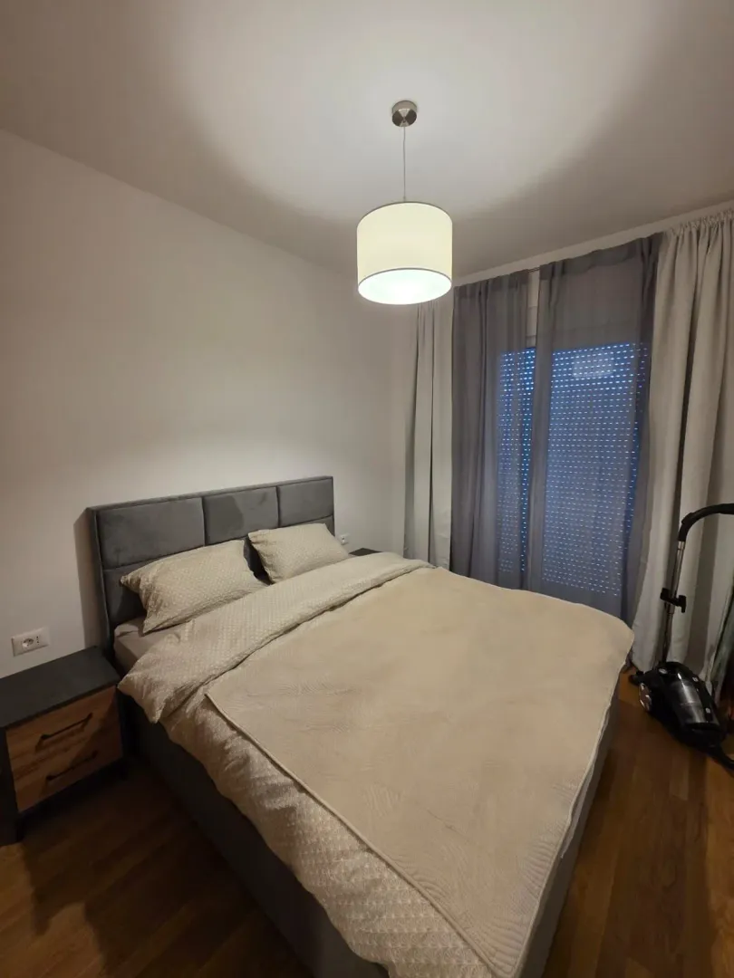 Spavaća soba sa bračnim krevetom, noćnim ormarićem i prozorom sa zavjesama.