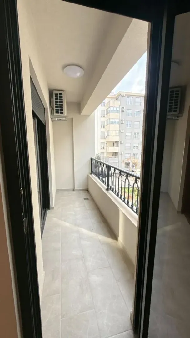 Pogled na prostrani popločani balkon sa crnom metalnom ogradom i spoljnom jedinicom klima uređaja.