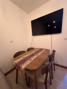 Dining area with a wooden table, chairs, and a large TV on the wall. - image 3