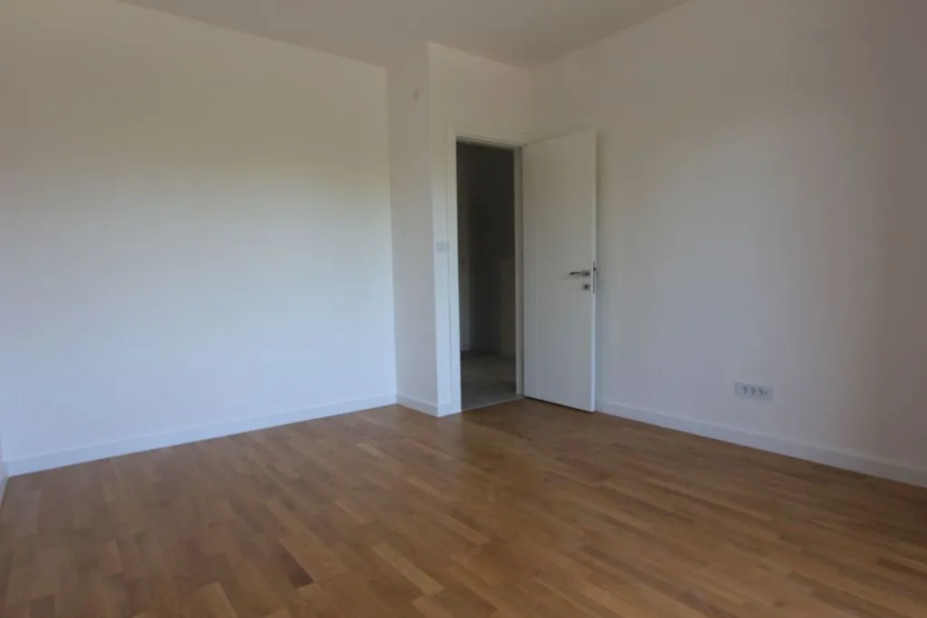 Prazna soba sa bijelim zidovima i drvenim podom.
