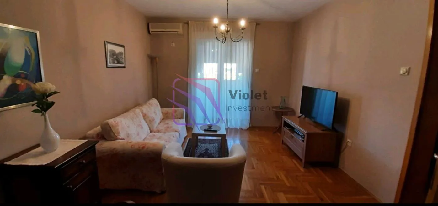 Dnevna soba sa garniturom, televizorom i izlazom na terasu.