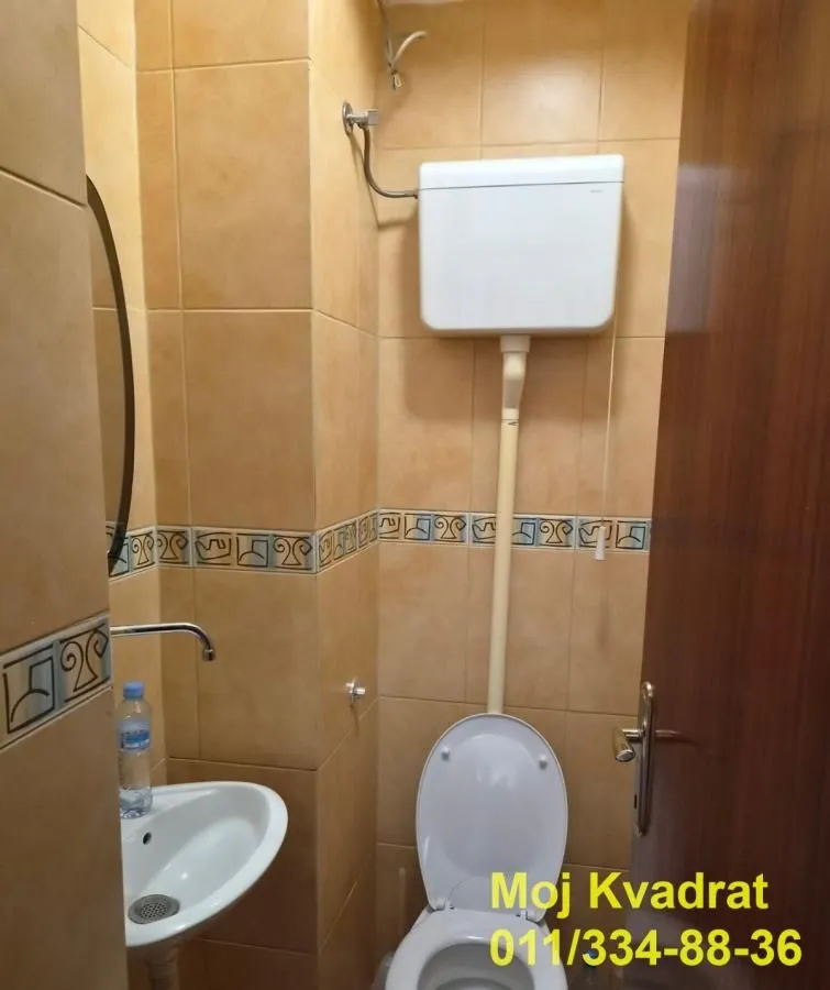 Manje kupatilo obloženo keramičkim pločicama sa umivaonikom i šoljom.
