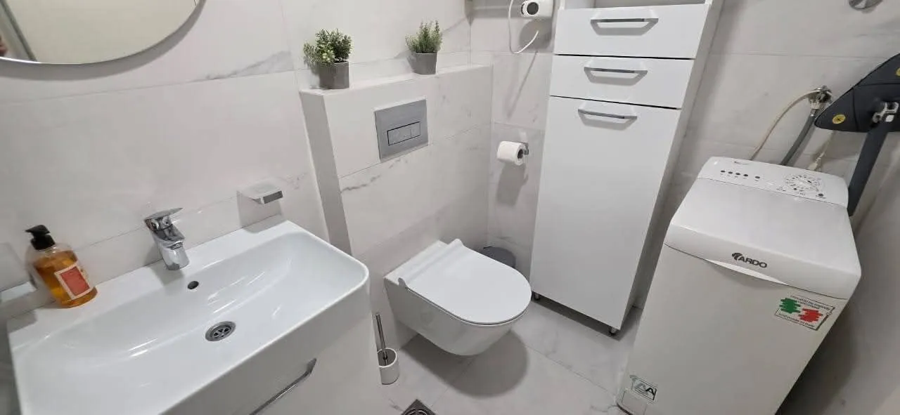 Moderne kupatilo sa umivaonikom, wc šoljom, ormarićem i mašinom za veš.