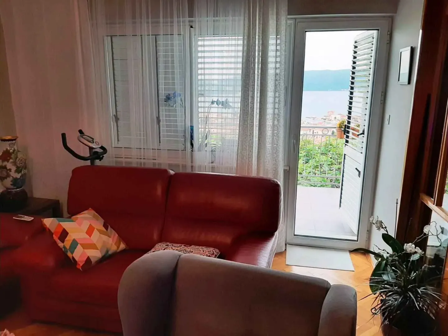 Dnevna soba sa crvenom kožnom garniturom i izlazom na balkon sa pogledom na more.