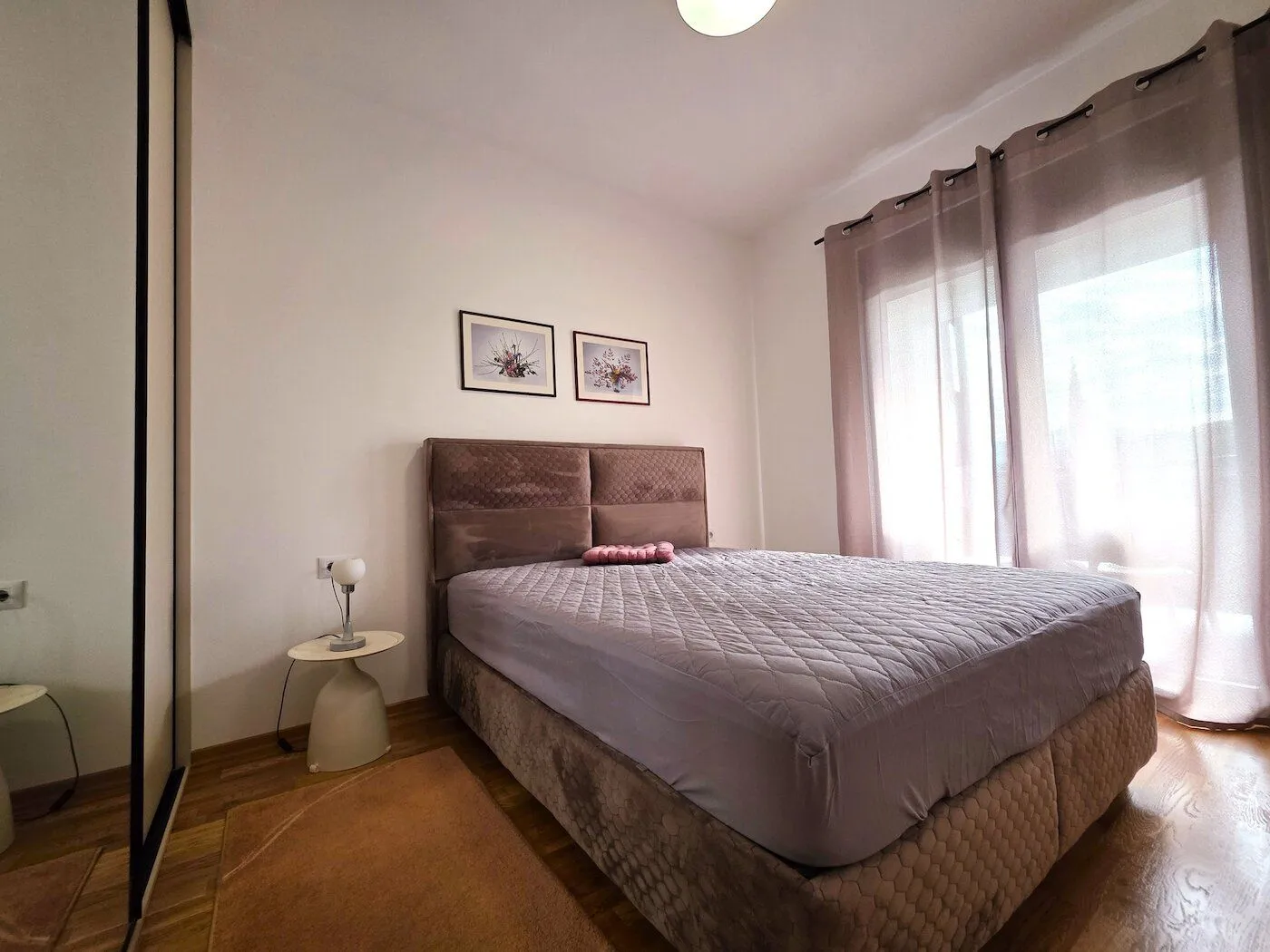 Furnished bedroom with a double bed, bedside table, and window with curtains.