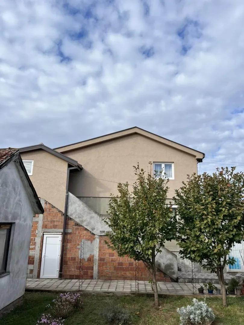 Vanjski dio dvospratne kuće sa dvorištem i ukrasnim drvećem.
