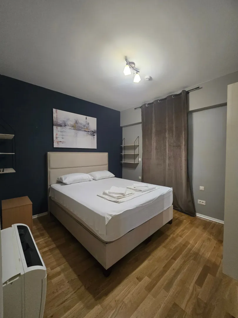Moderna spavaća soba sa bračnim krevetom, tamnim zidom i drvenim podom.