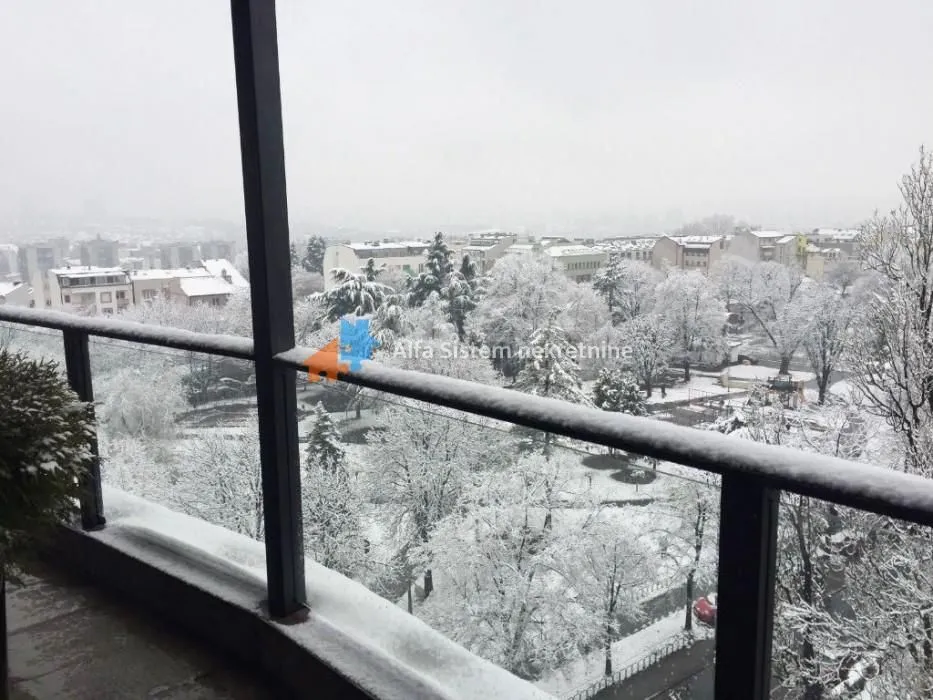 Pogled sa snežnog balkona na okolne zgrade i drveće.