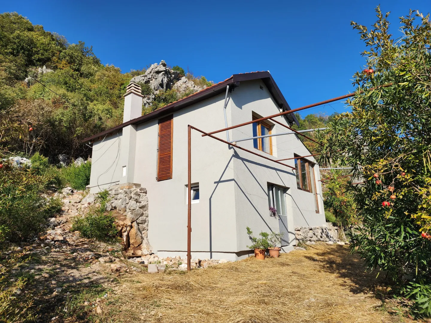 Pogled na spoljašnjost kuće sa dvorištem i brdovitom pozadinom.