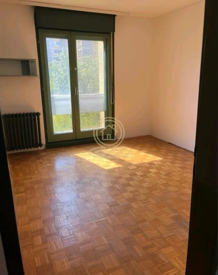 Prazna soba sa parketom i balkonskim vratima.