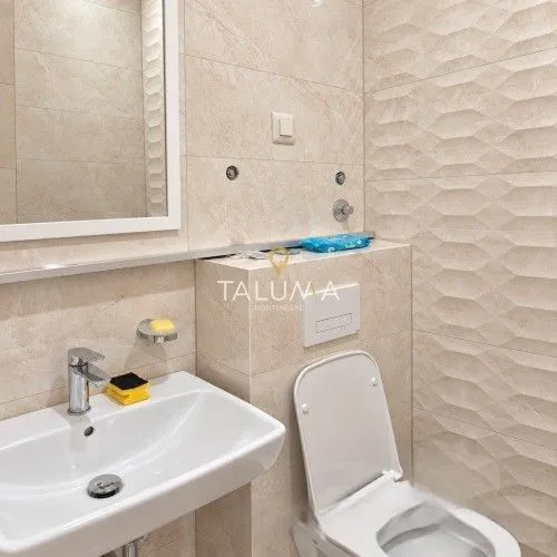 Smaller bathroom with a sink, mirror, and toilet lined with ceramic tiles.