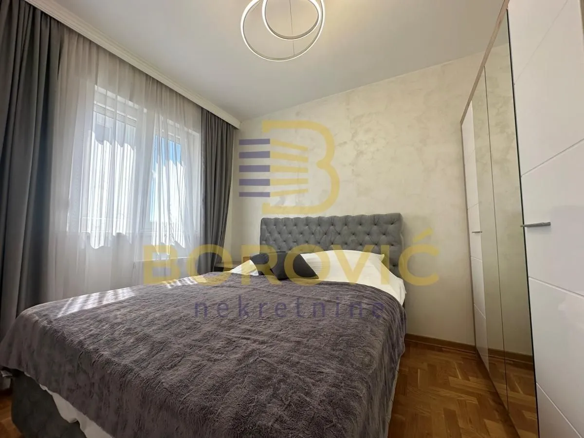Nameštena spavaća soba sa bračnim krevetom, ormarom i prozorom.