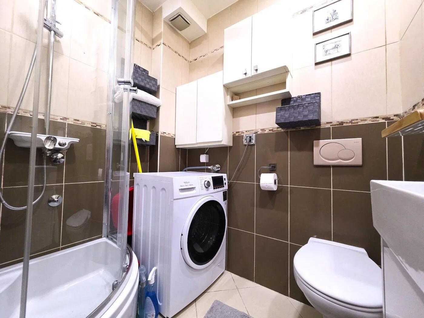Smaller bathroom equipped with a shower cabin, sink, toilet, and washing machine.