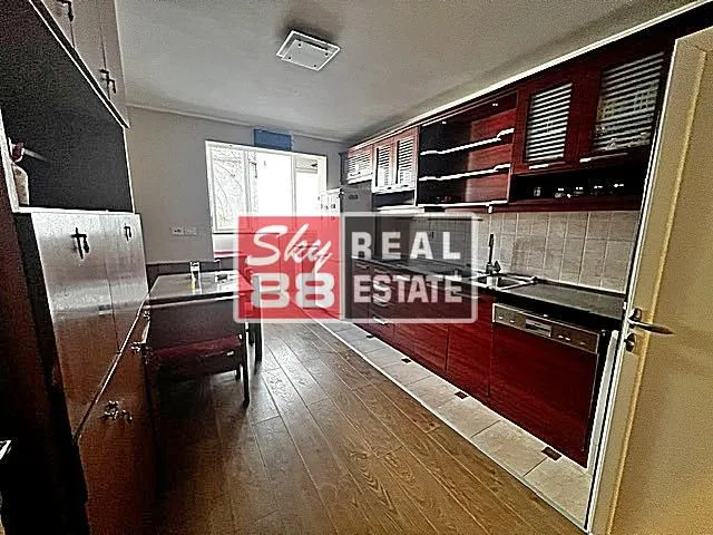 Long kitchen with dark wooden cabinets and a dining table in the background.