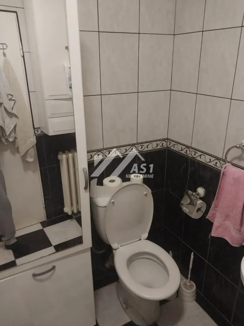 Manje kupatilo sa WC šoljom, pločicama i ugradnim elementima.