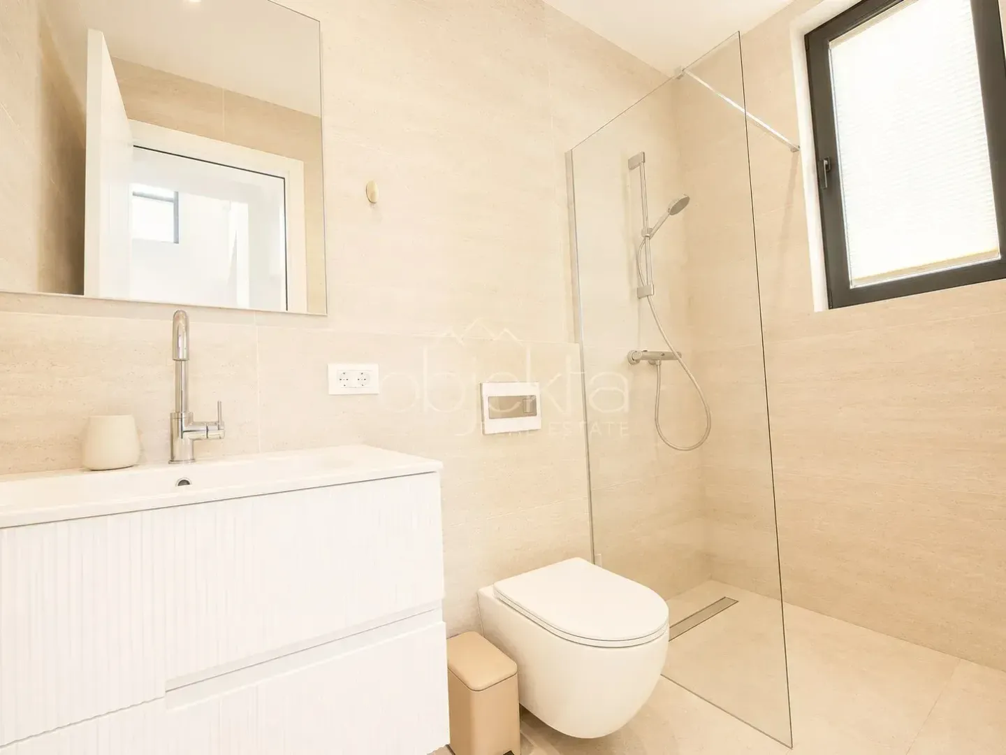 Modernly equipped beige-toned bathroom with a walk-in shower and white sink.