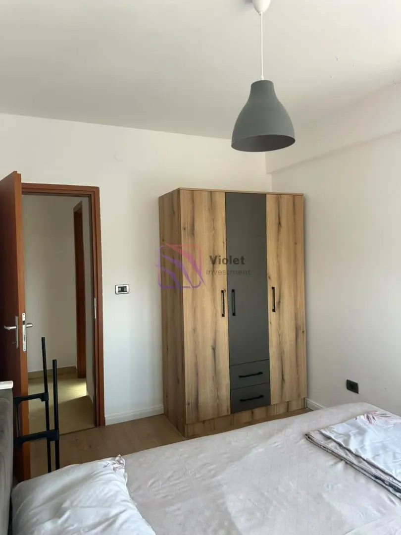 Namještena spavaća soba sa krevetom, drvenim ormarom i lusterom.