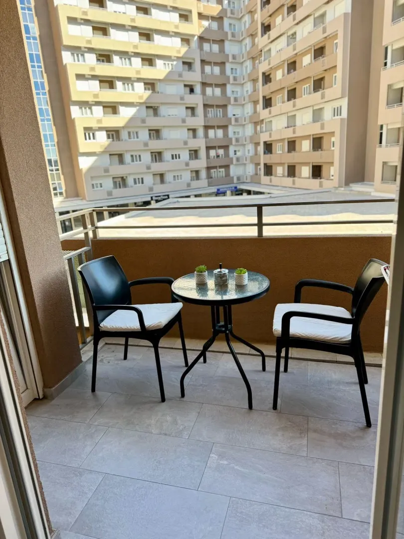 Namješten balkon sa stolom i dvije stolice i pogledom na zgradu.
