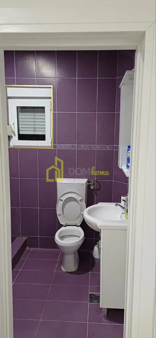 Small bathroom with purple tiles, toilet, and vanity with sink.