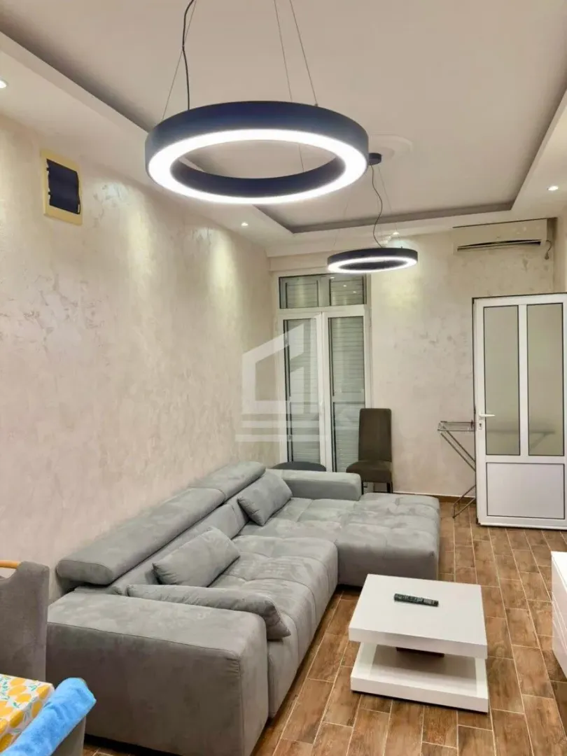 Dnevna soba sa ugaonom garniturom, stočićem i modernim visećim lampama.