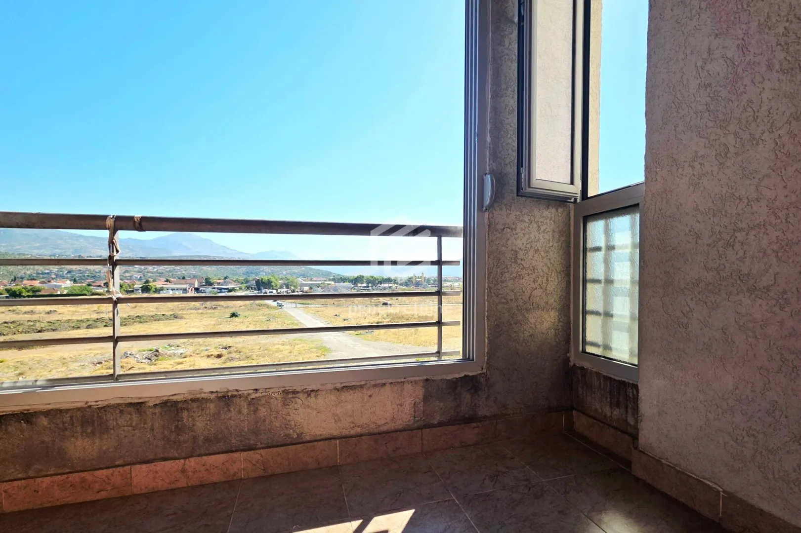 Natkriveni balkon sa metalnom ogradom i pogledom na okolni krajolik.