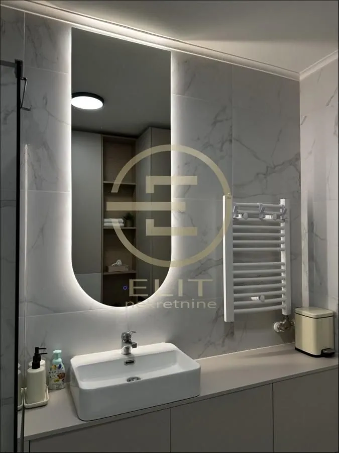 Moderno opremljeno kupatilo sa umivaonikom i osvetljenim ogledalom.