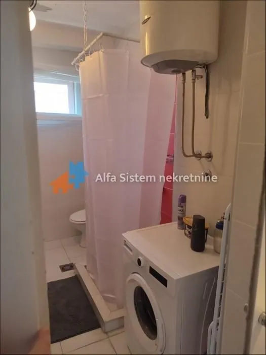 Manje kupatilo sa tuš kabinom, bojlerom i veš mašinom.