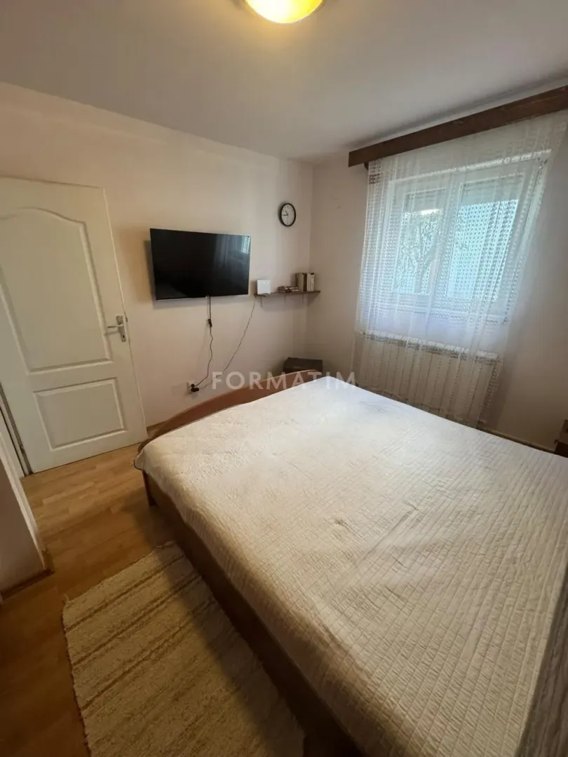 Nameštena spavaća soba sa bračnim krevetom, televizorom i prozorom.