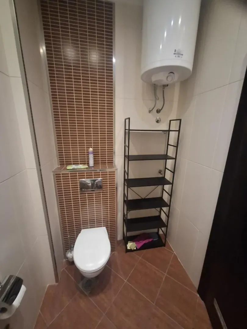Manje kupatilo sa wc šoljom, bojlerom i metalnom policom.
