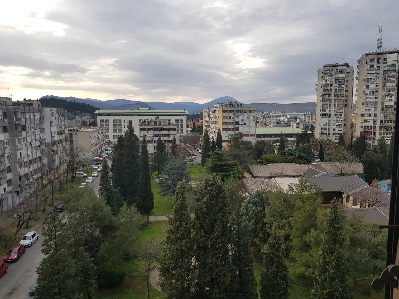 View from a high floor overlooking surrounding buildings, a park, and mountains in the distance.