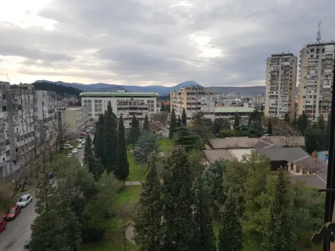 View from a high floor overlooking surrounding buildings, a park, and mountains in the distance. - image 10
