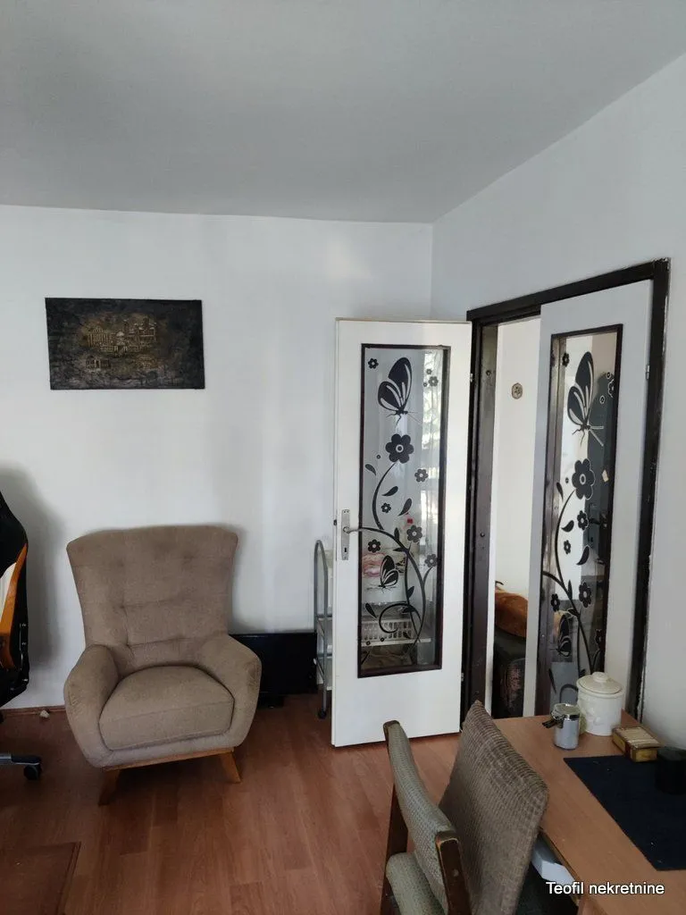 Dnevna soba sa foteljom, radnim stolom i dekorativnim vratima.