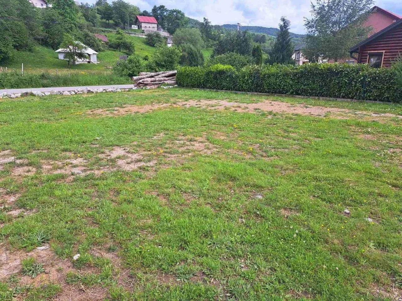 Prostrani travnati plac okružen prirodnim pejzažom i kućama.