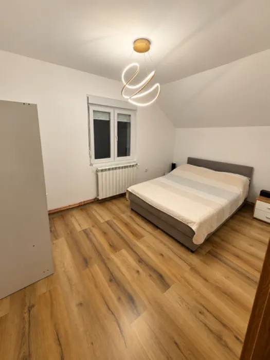Spavaća soba sa bračnim krevetom, ormarom i modernim lusterom.