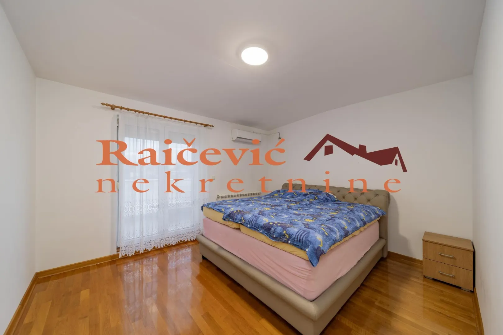 Nameštena spavaća soba sa bračnim krevetom i izlazom na balkon.