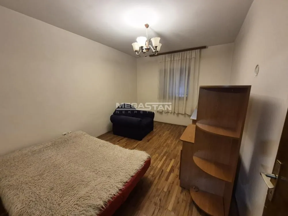 Nameštena spavaća soba sa bračnim krevetom, foteljom i drvenim ormanom.