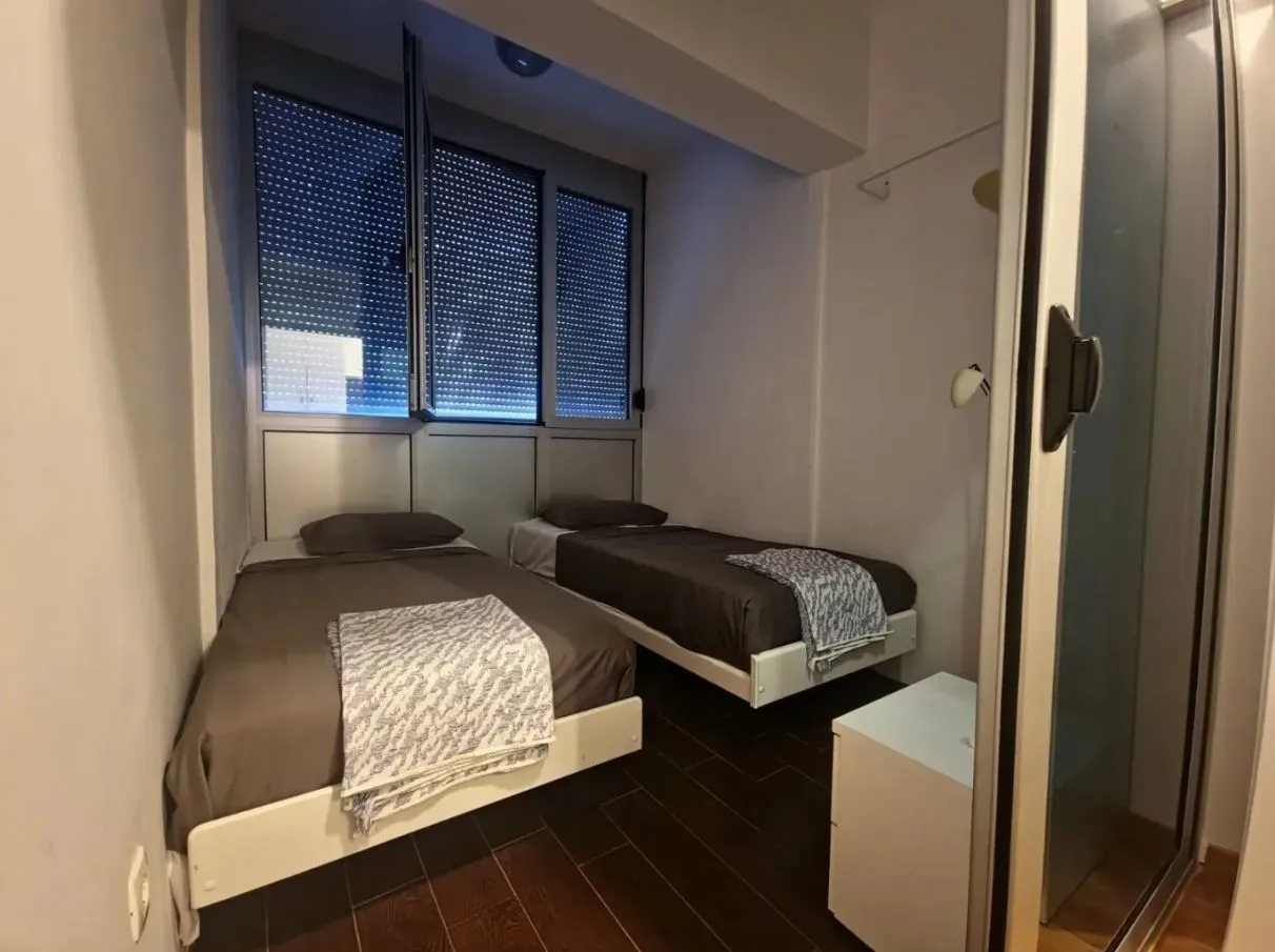 Manja spavaća soba sa dva singl kreveta i tamnim parketom.