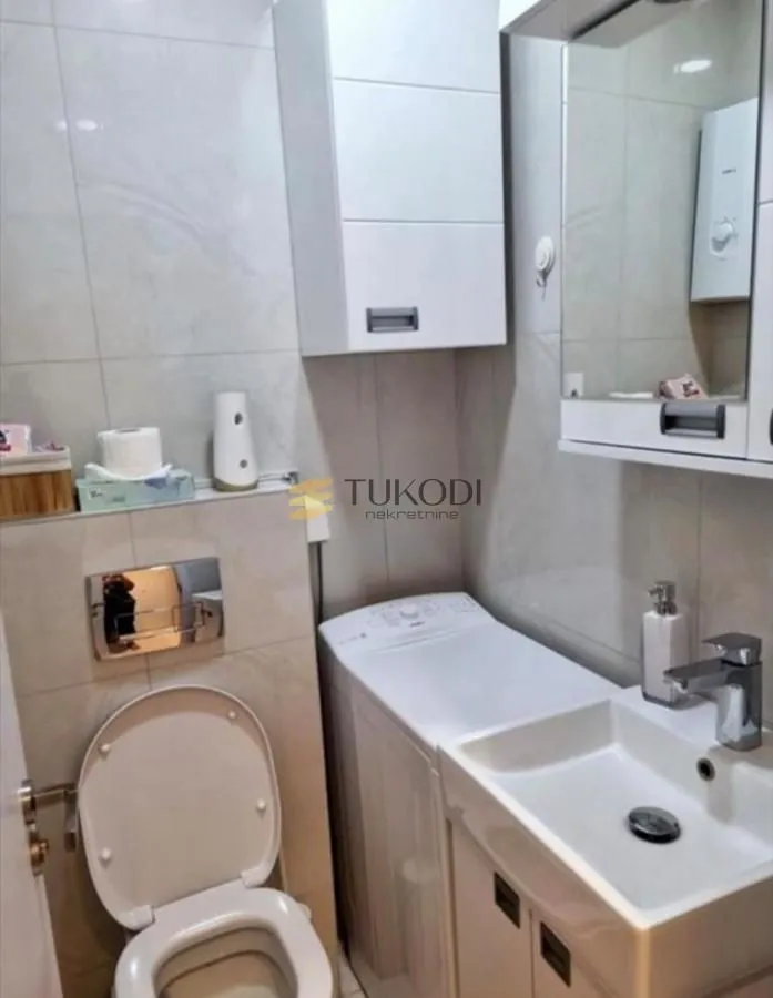 Smaller bathroom with a washbasin, toilet, washing machine, and wall cabinets.
