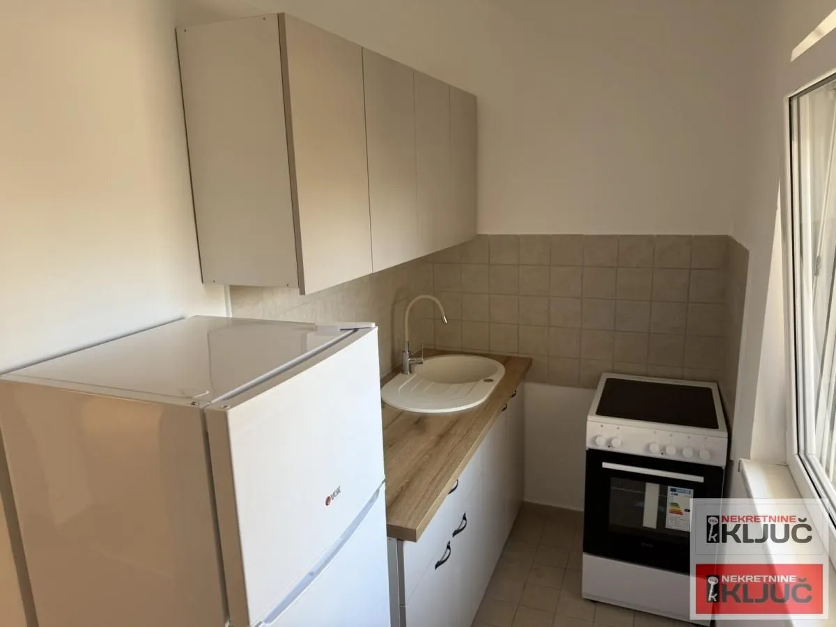 Manja kuhinja opremljena osnovnim elementima, šporetom i frižiderom.