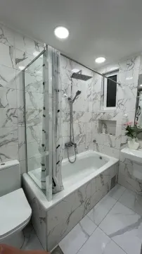 Moderne kupatilo obloženo mermernim pločicama sa kadom i paravanom za tuširanje. - image 4