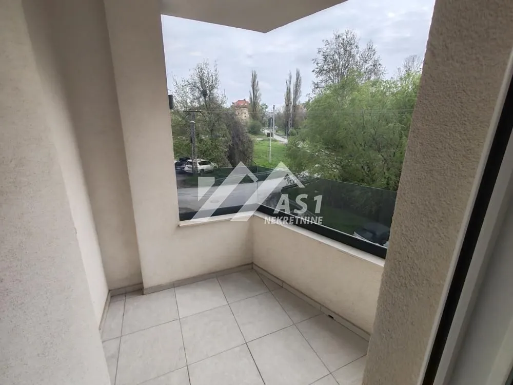 Nenameštena terasa sa staklenom ogradom i pogledom na zelenilo.