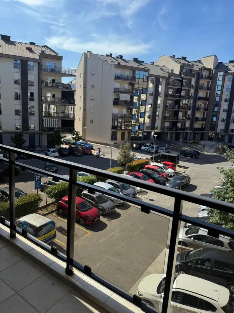 Pogled sa balkona na stambene zgrade i parking.