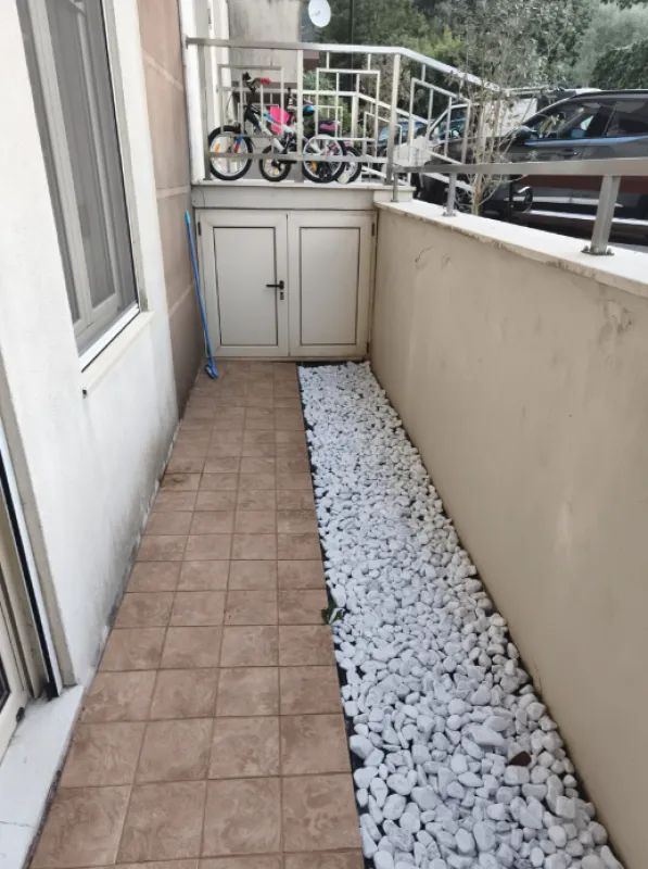 Popločani spoljašnji prostor sa bijelim šljunkom i ostavom pored zgrade.
