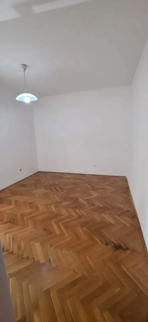 Prazna soba sa drvenim parketom i bijelim zidovima.