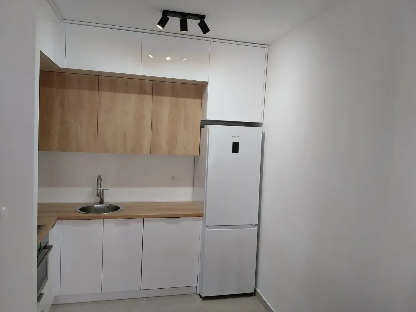 Modern white kitchen with wooden elements and a refrigerator.